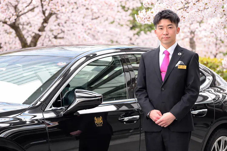 Professional chauffeur standing beside a luxury car during cherry blossom season in Japan