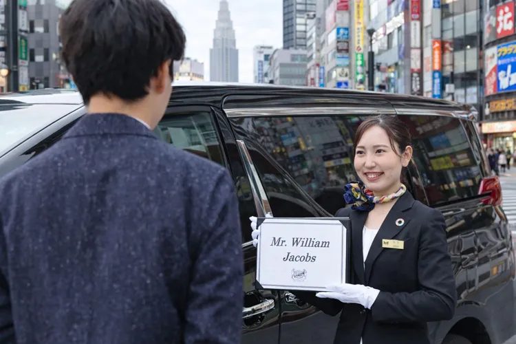 A professional chauffeur greeting a passenger with a name sign beside a luxury vehicle in Tokyo